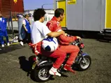 Nigel Mansell gives his Scuderia Ferrari co-driver Alain Prost a ride on his Honda ST-70 motorbike at the 1990 British Grand Prix, which Prost won.