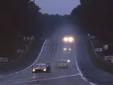 The Jaguar XJ220 C LM driven by Richard Piper, Tiff Needell, and James Weaver leads down the hill as night falls on the 1995 24 Hours of Le Mans.