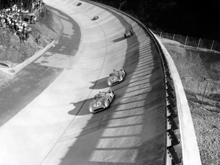 Italian Grand Prix in Monza, 11 September 1955: Stirling Moss (starting number 16) leads the steep bend ahead of the winner Juan Manuel Fangio (starting number 18), both in Mercedes-Benz W 196 R with streamlined bodywork, followed by Piero Taruffi (2nd place) in a Mercedes-Benz W 196 R Monoposto (starting number 14).