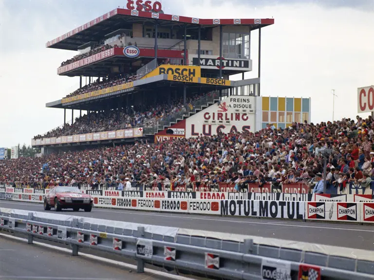 Chassis 12467 thunders along the pit straight, V-12 howl delighting fans in a packed main grandstand.